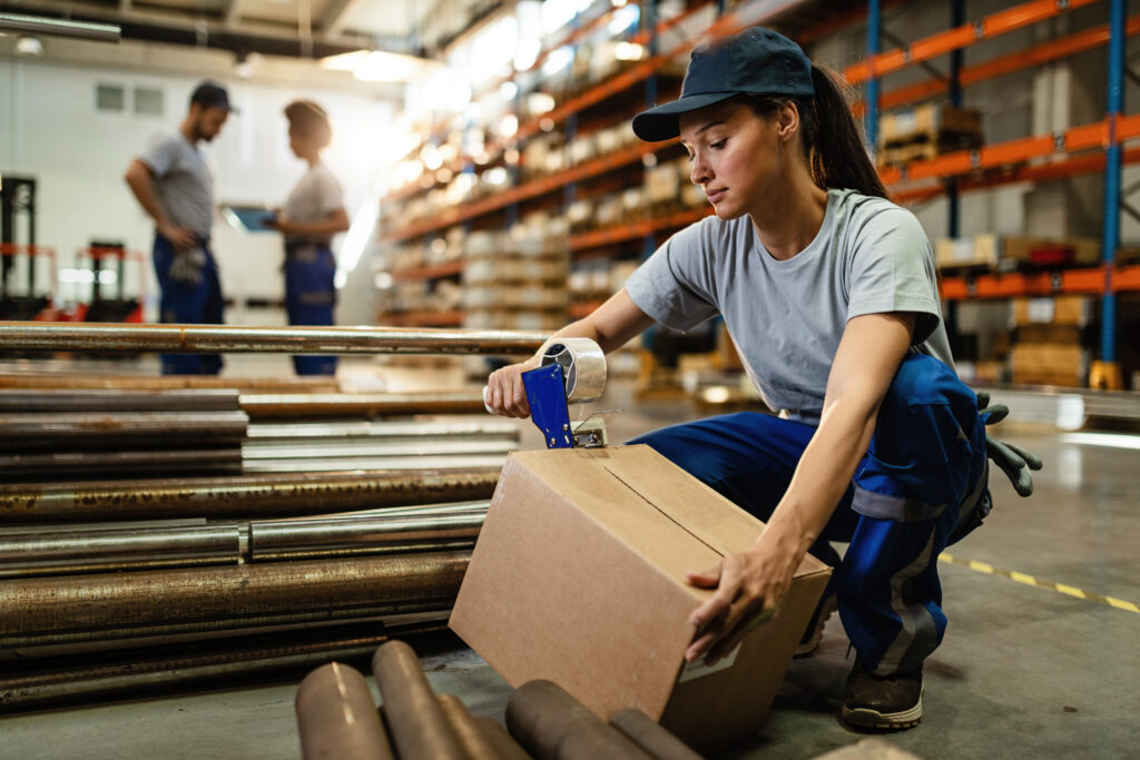 young woman working in warehouse and taping cardboard box for shipment.